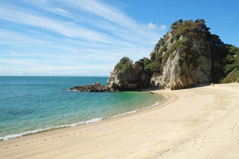 sandy beach next to calm turquoise sea blocked by vegetated boulders