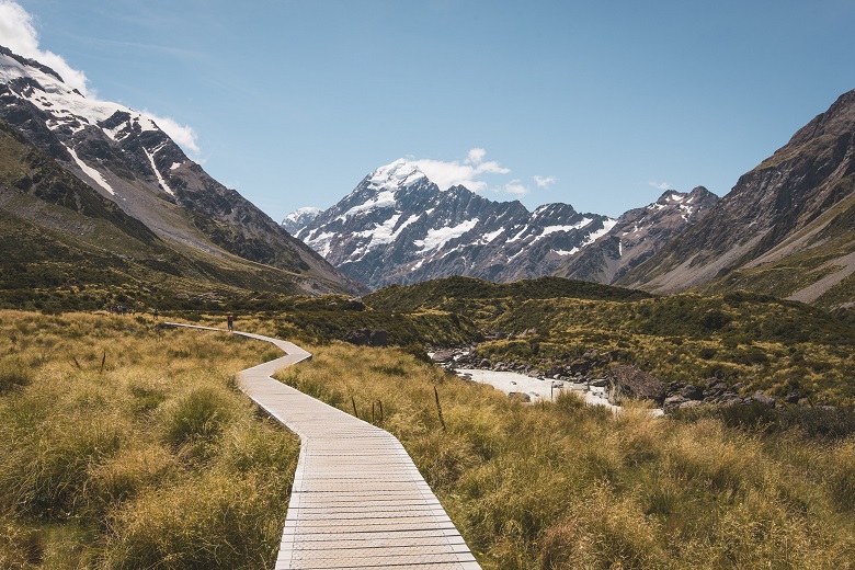 boardwalk through meadow valley toward snowy mountain peaks