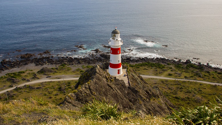 red and white lighthouse on a promontory above the ocean