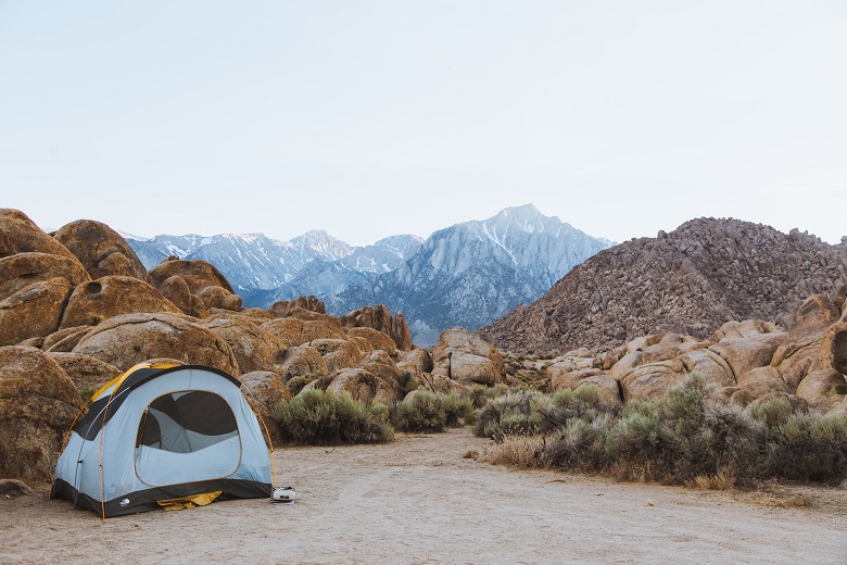 Tent on flat dirt area among boulders with snow mountain peaks in the background