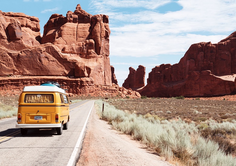 yellow campervan on desert road surrounded by red sandstone cliffs