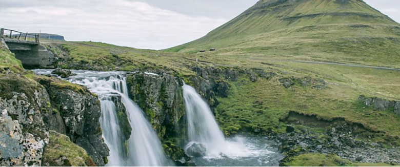 Bridge over 2 waterfalls with a mountain in the background