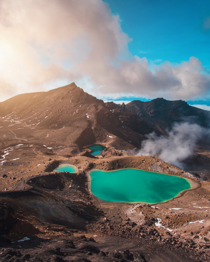 three alpine ponds surrounded by brown sand and rocks and clouds