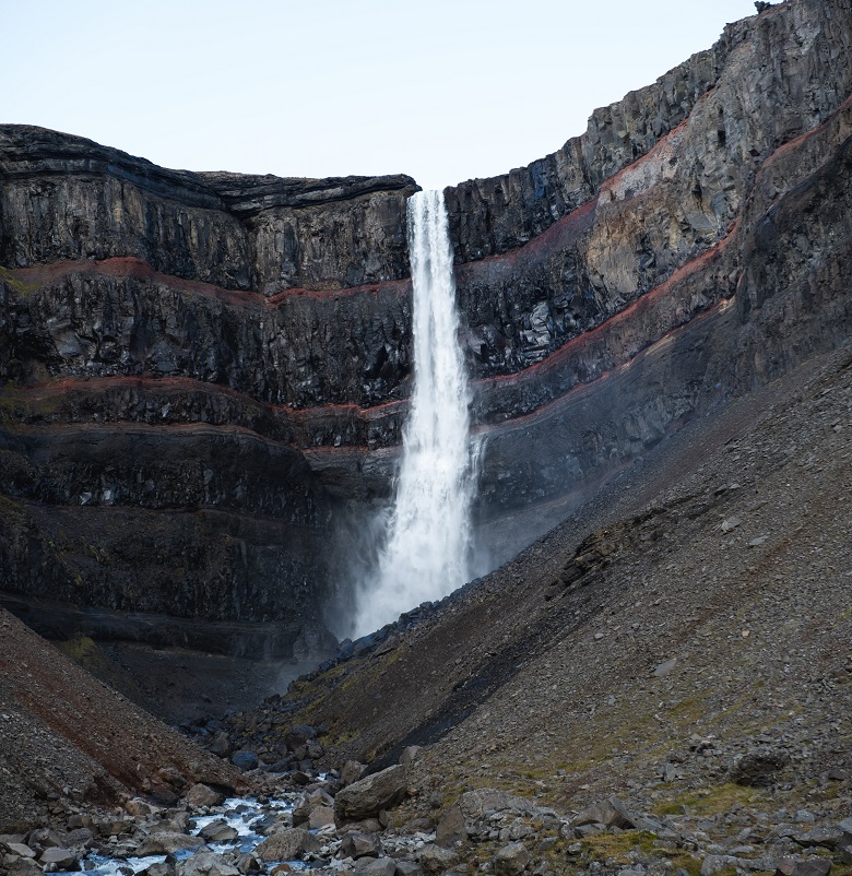 Thin waterfall falling over grey cliff face with red horizontal stripes
