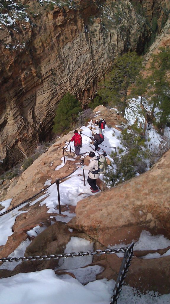 people hiking down steep snowy path marked by chains