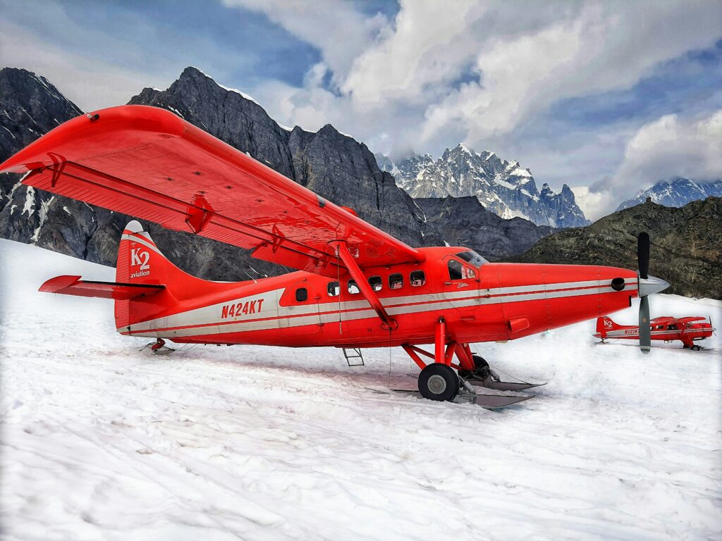 2 small red planes on snow with mountain peaks in the background