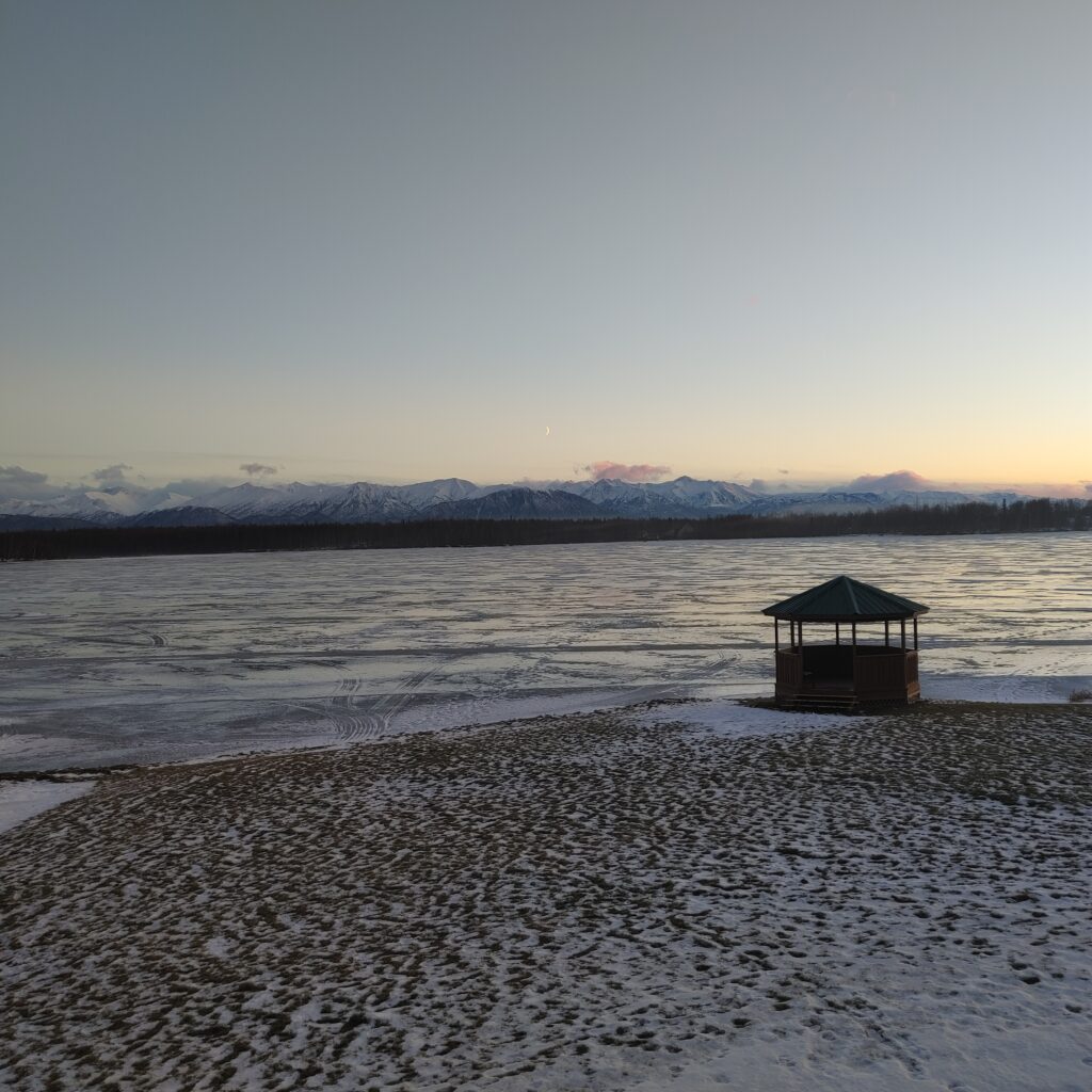 mountain range behind frozen lake with gazebo on beach