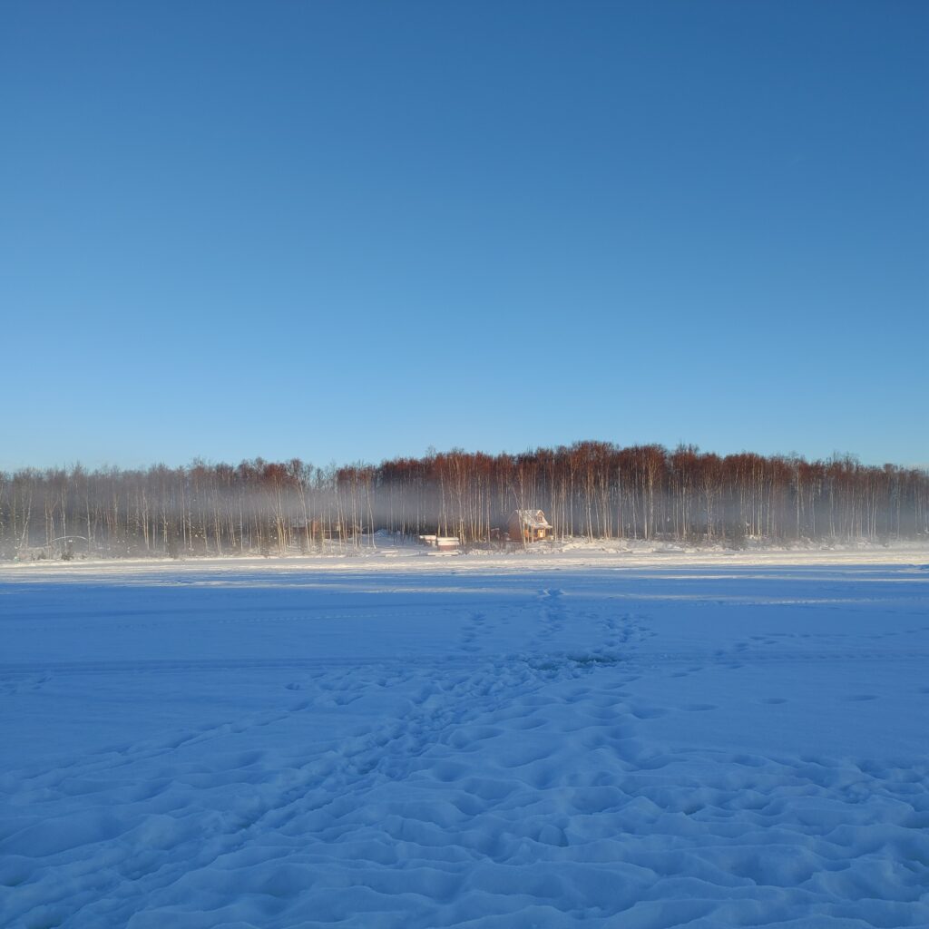 footprints on frozen lake leading to house at shore